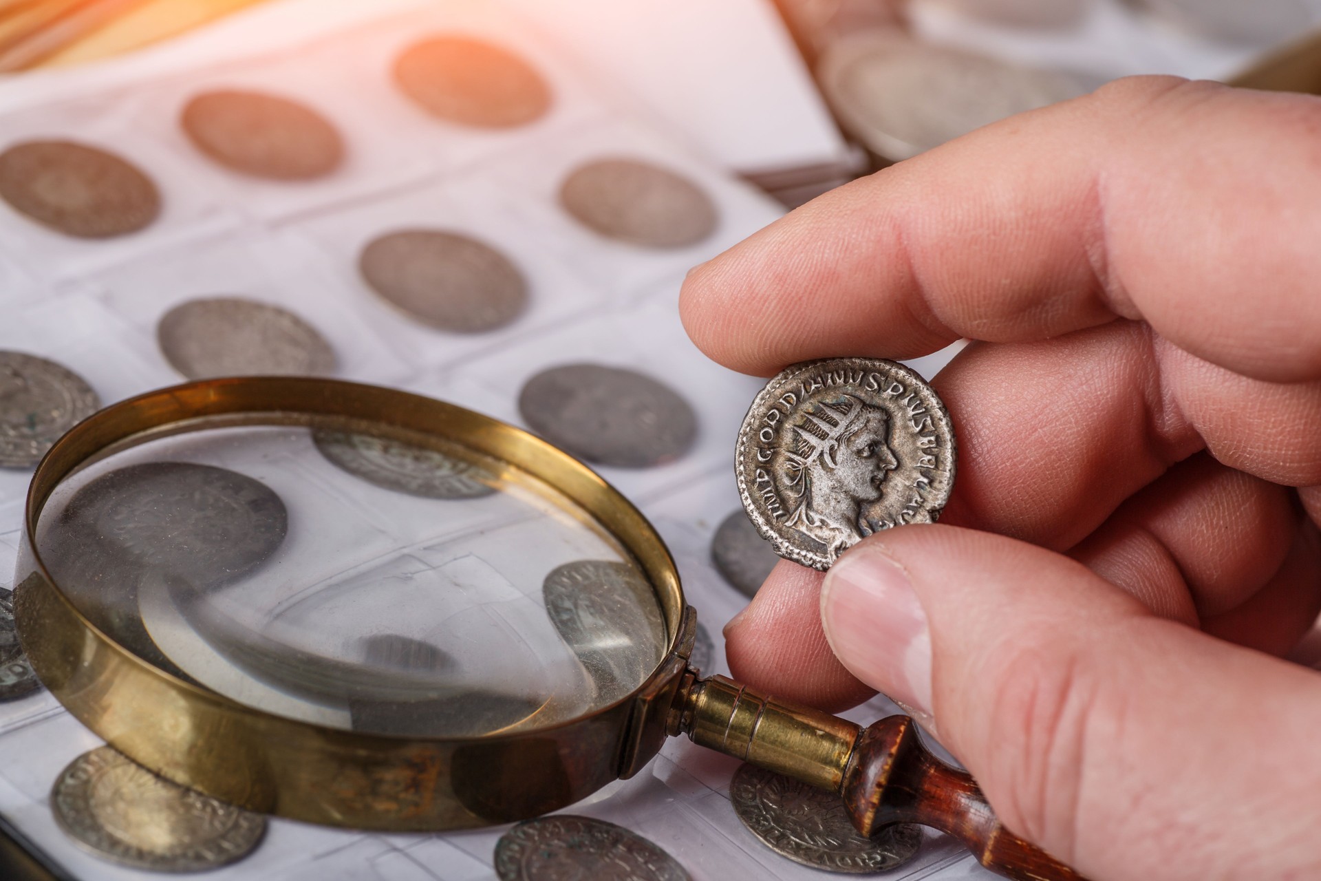 Numismatics. Old collectible coins made of silver on a wooden table. A collector holds an old coin. Ancient coin of the Roman Empire.